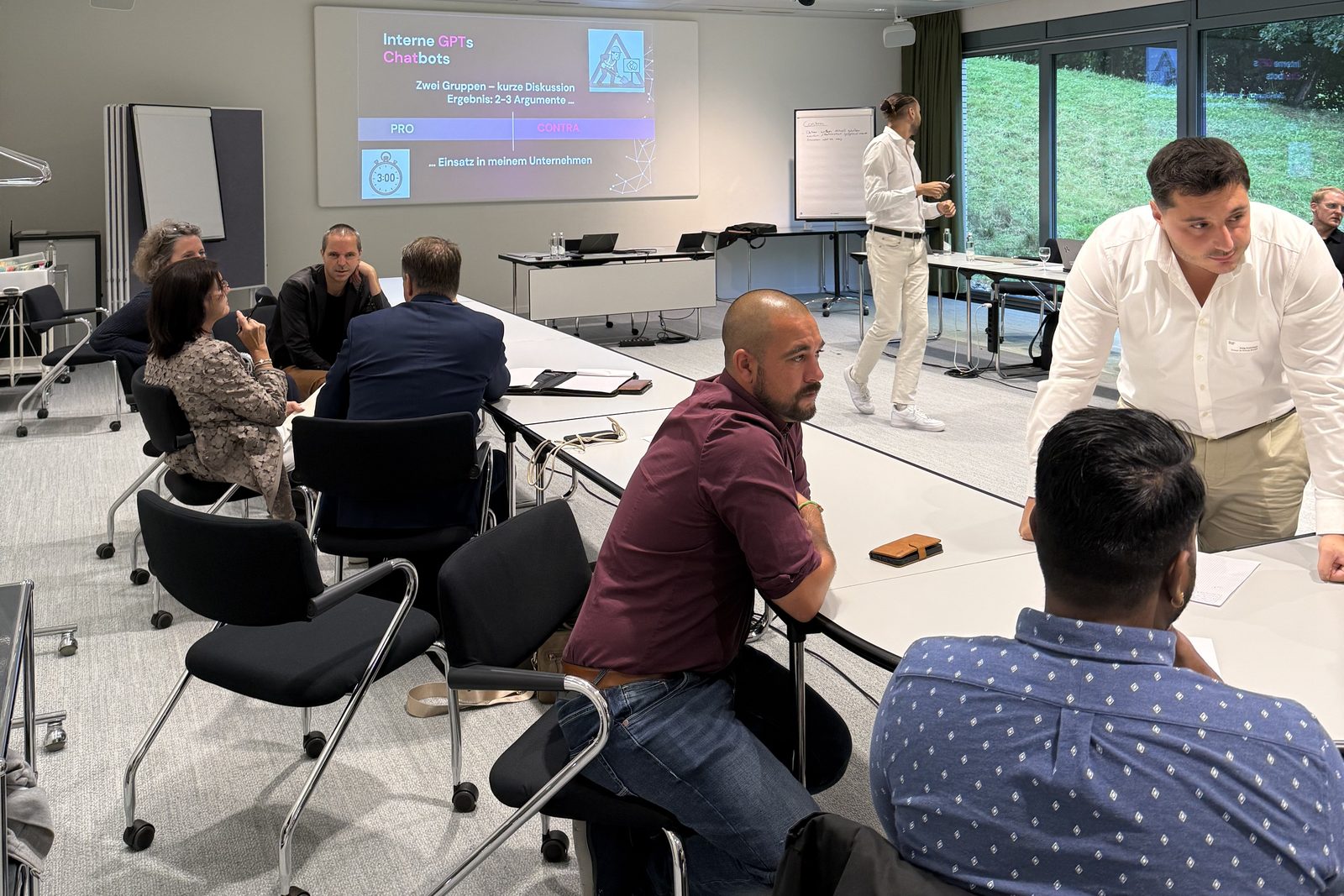 Participants à l'atelier discutant en groupes, avec à l'écran la consigne sur les GPT et chatbots internes